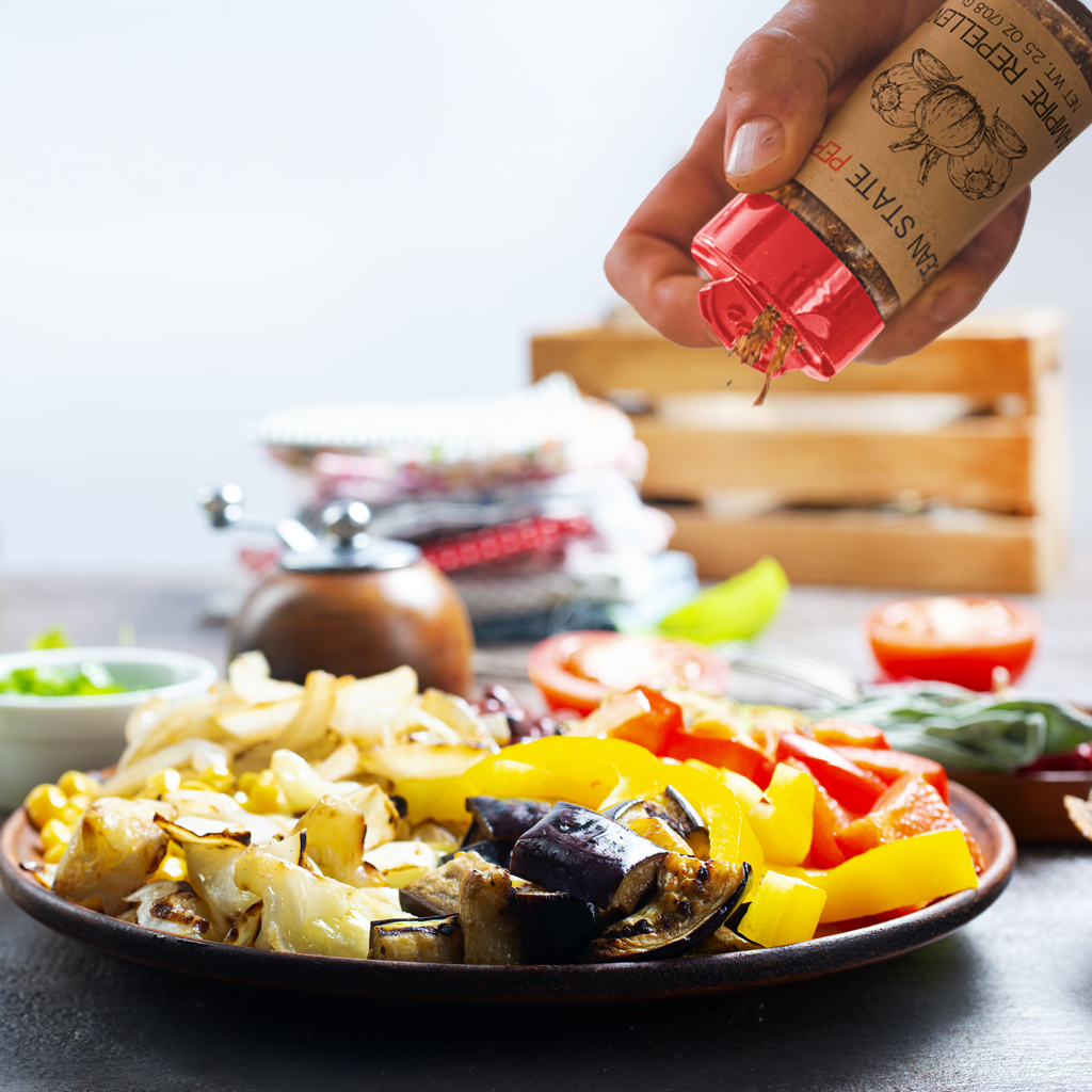 Person seasoning a plate of vegetables with a spice container on a blurred background