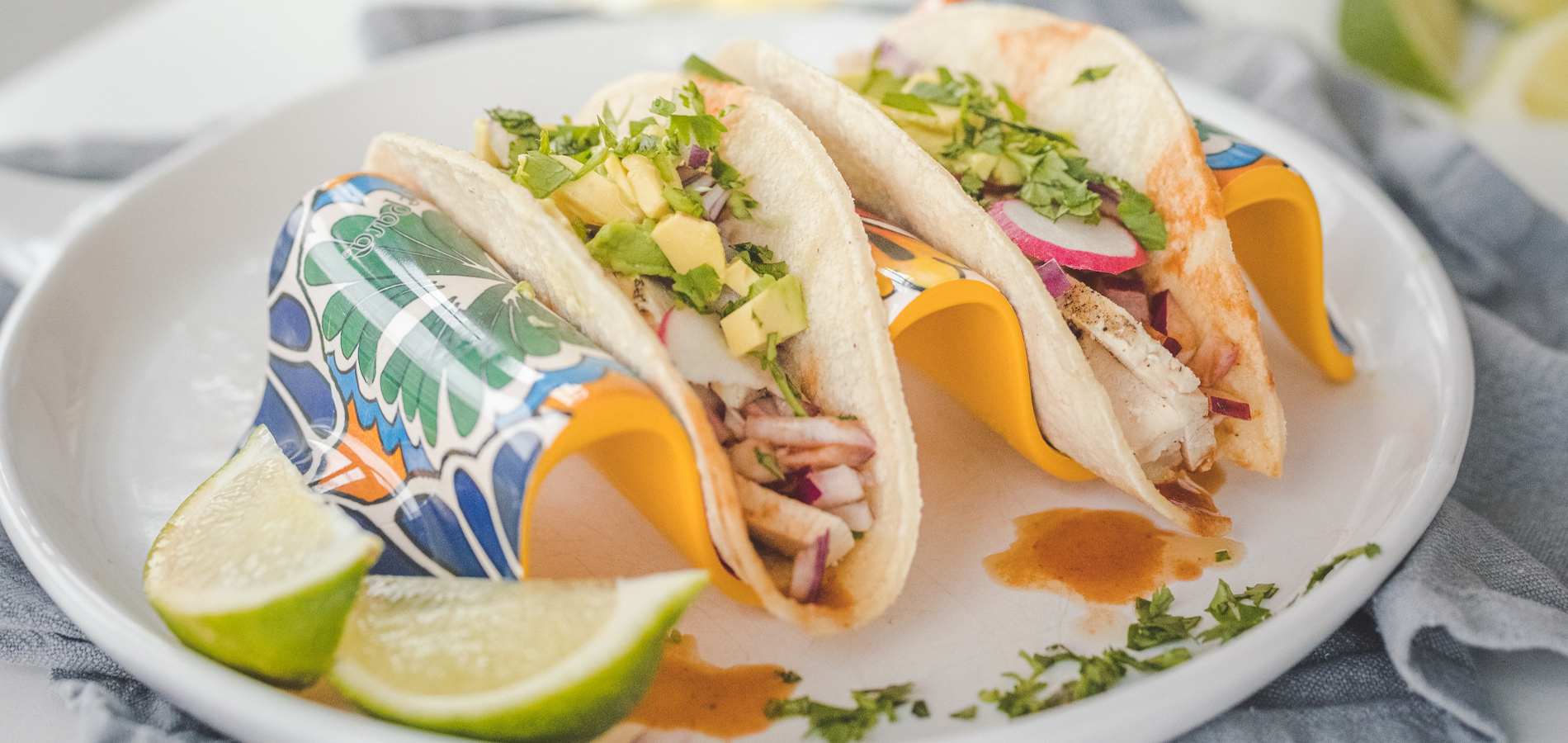 Three tacos with various fillings on a decorative plate with lime wedges.