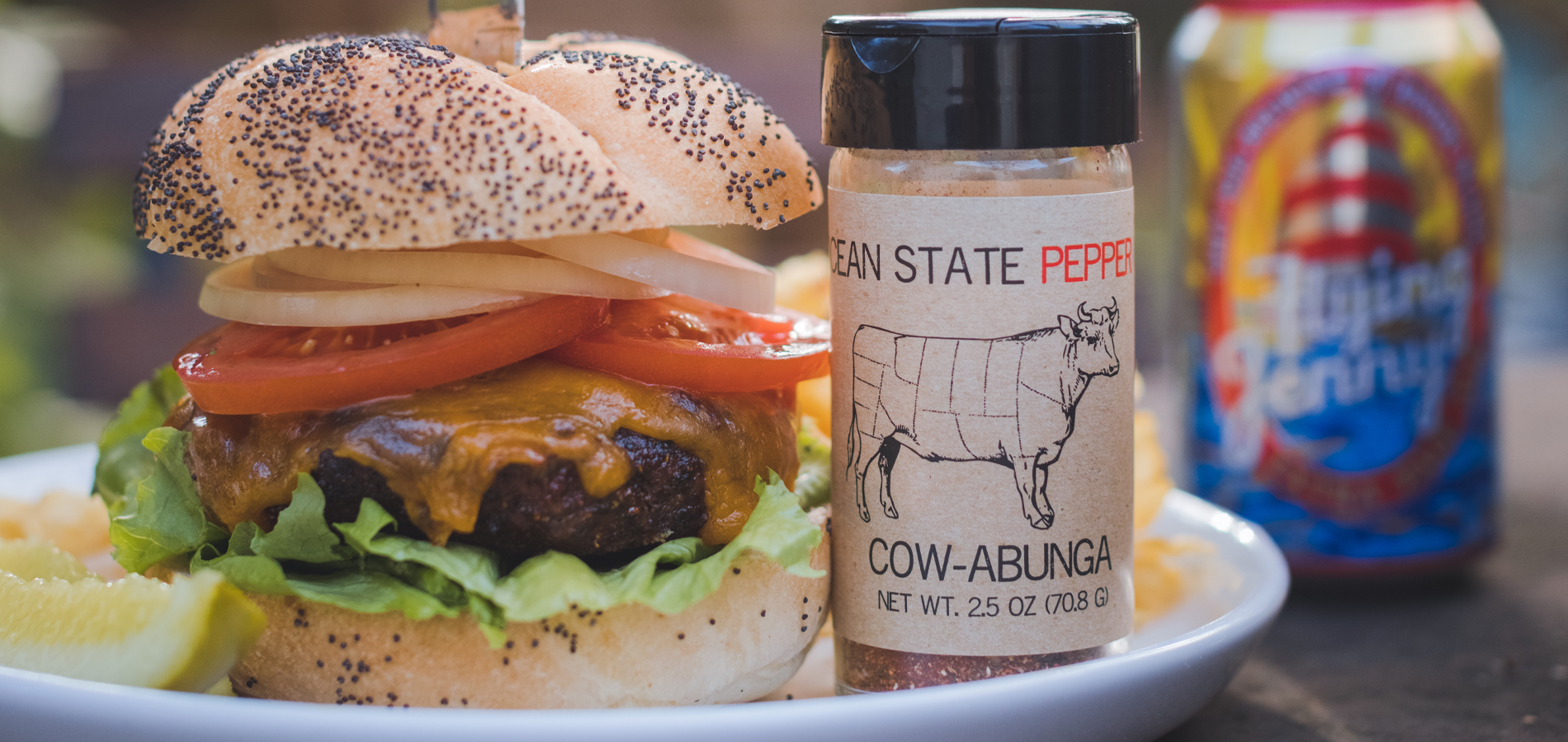 Hamburger on a plate with a jar of 'Cow Abunga' seasoning and a can of beer in the background.