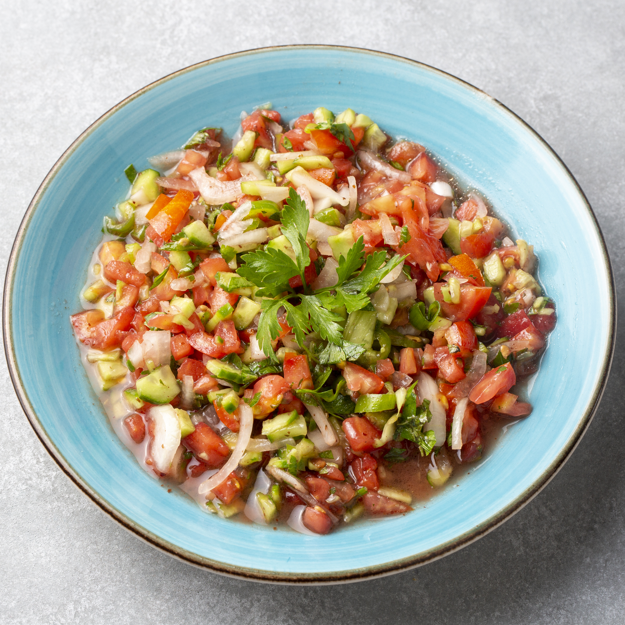Colorful salad with tomatoes, cucumbers, and onions in a blue bowl on a light gray background